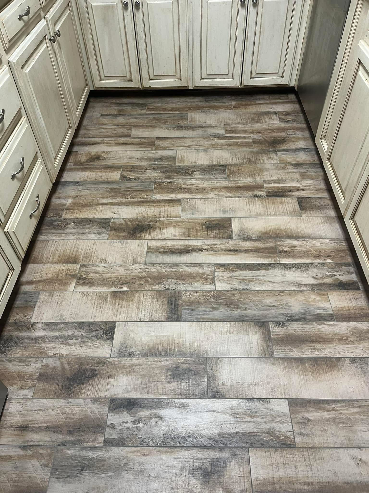 Wooden-look flooring in a kitchen with white cabinets. The floor is composed of rectangular planks in shades of brown, gray