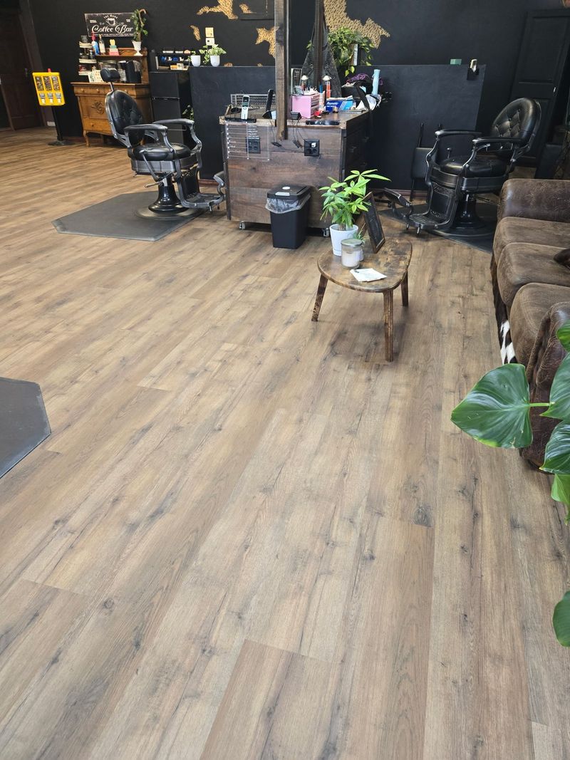 A barber shop interior with wooden floors, chairs, and styling stations.