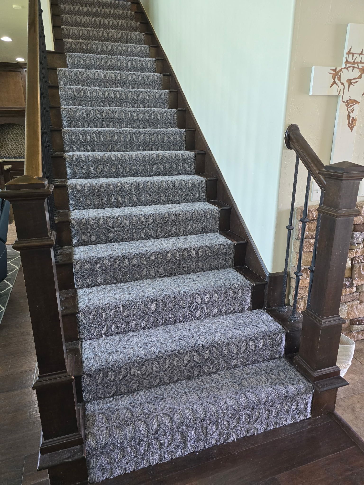 Staircase with dark wood and gray carpet. A wooden railing runs along the right side. A white wall is to the right.