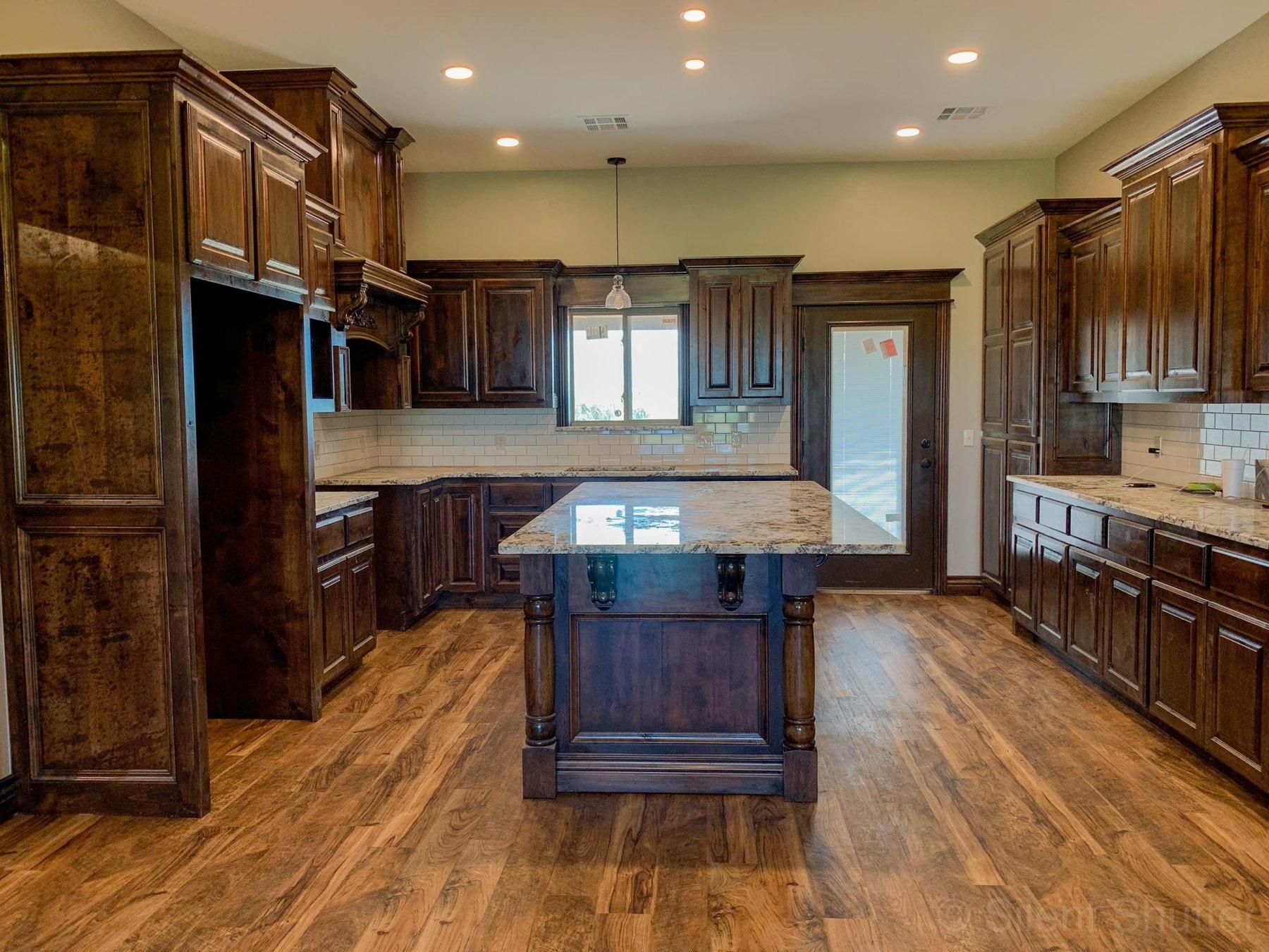 Spacious kitchen with dark wood cabinets, a central island, and wood-look flooring.  Neutral walls and countertops.