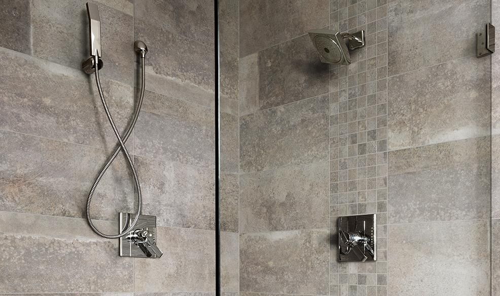 Shower with a handheld showerhead, faucet, and glass door. Gray tile walls, chrome fixtures.