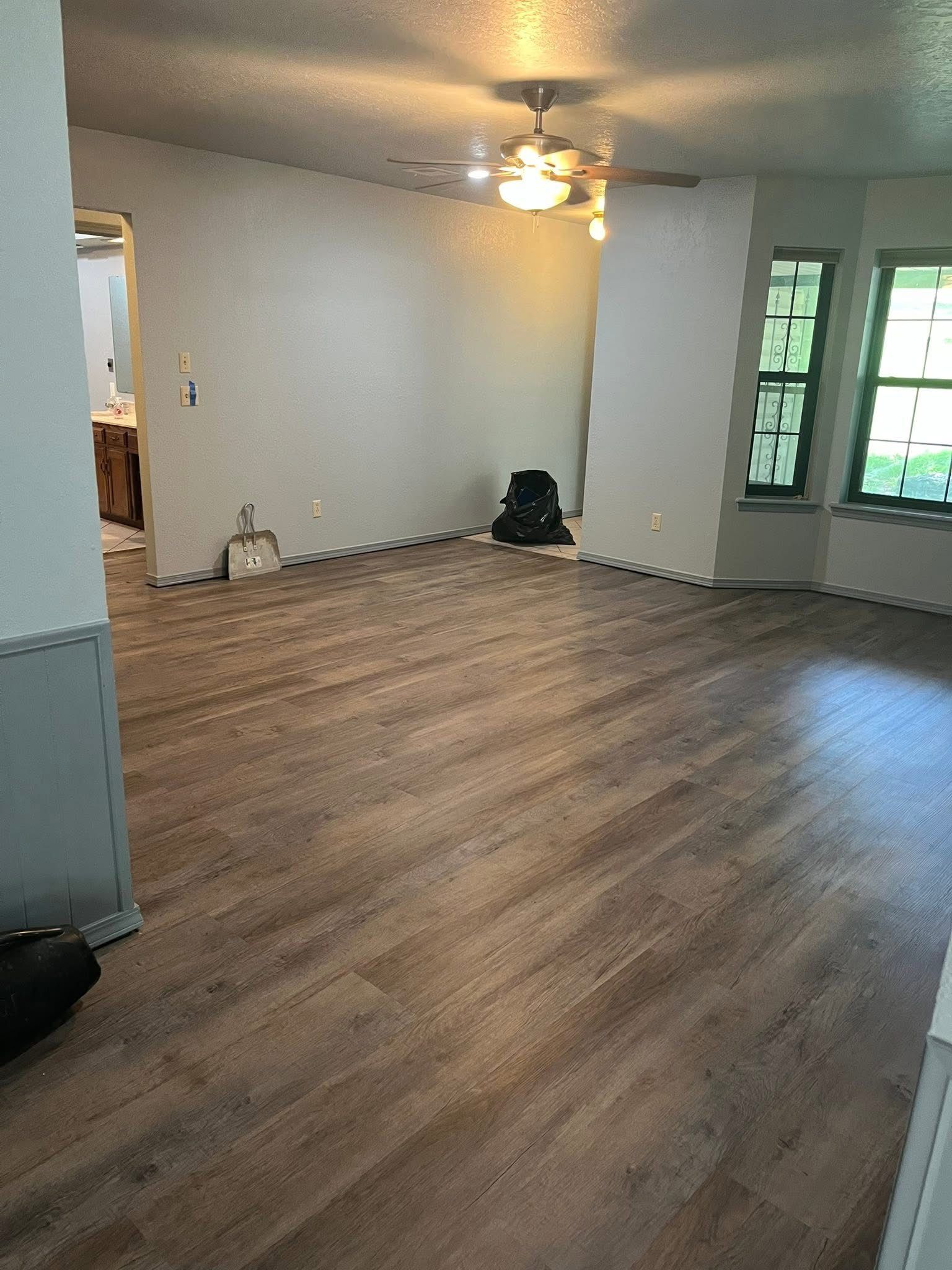 Newly installed wood-look flooring in a room with white walls, a ceiling fan, and a window.