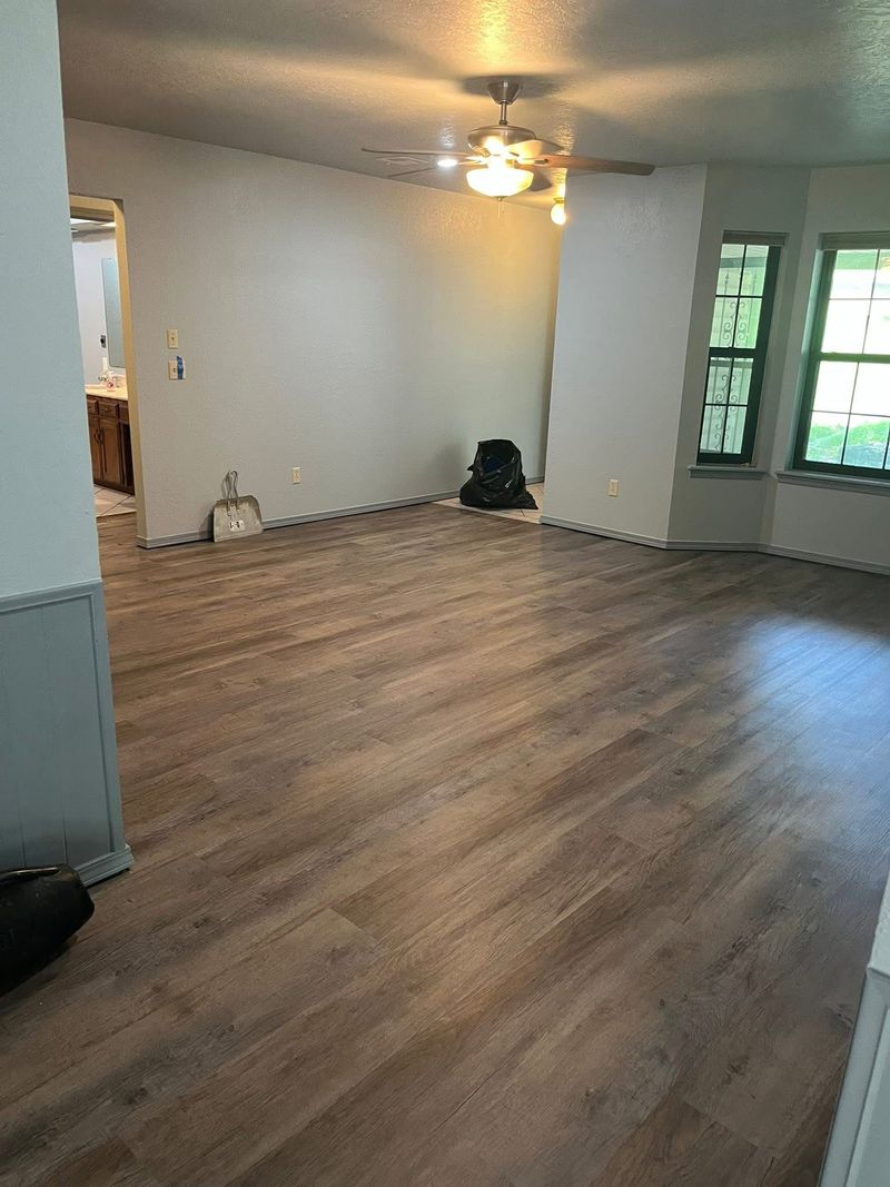 Empty living room with wood-look flooring, white walls, and a ceiling fan.
