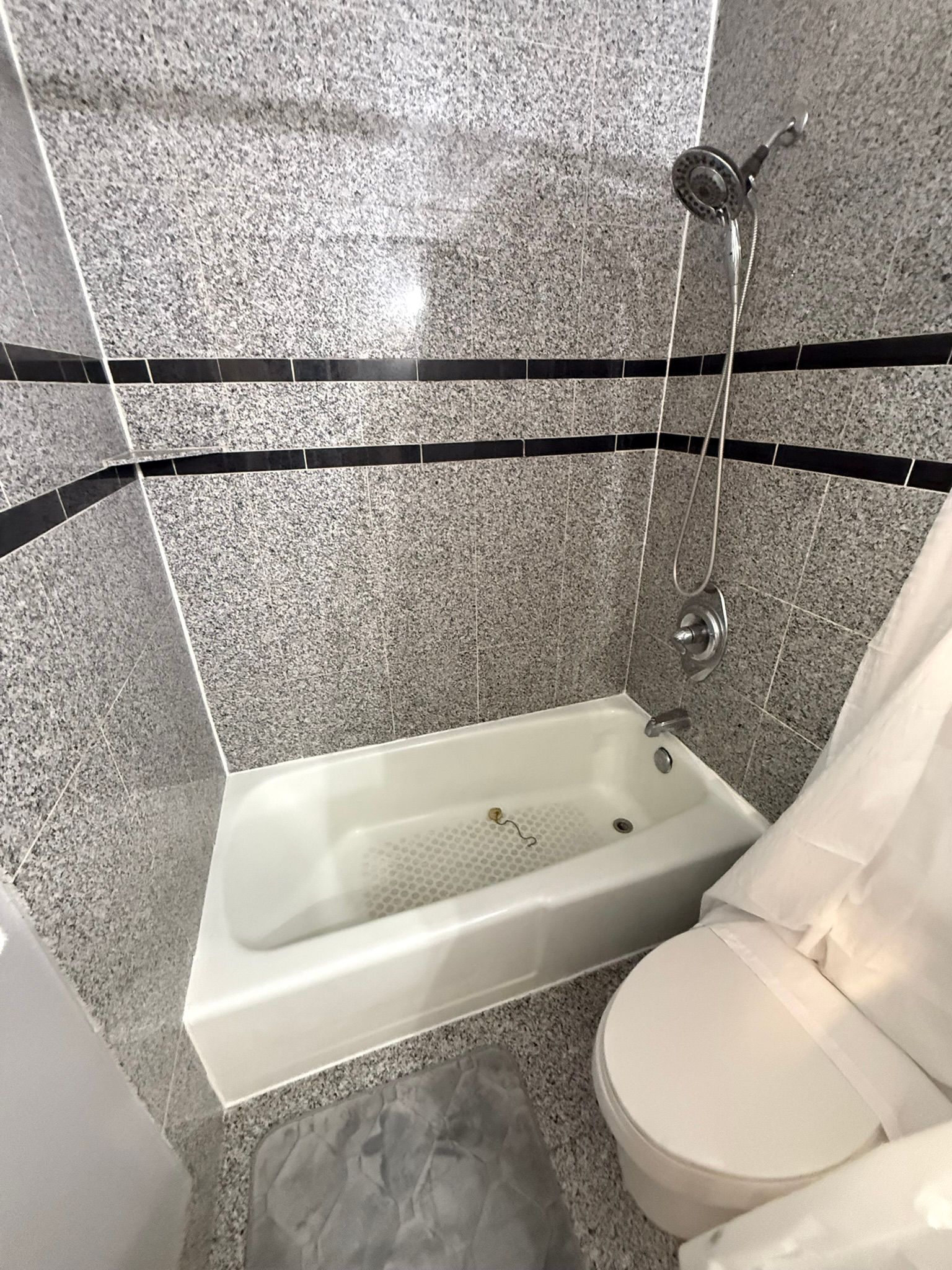 Small bathroom with a white tub, toilet, and a speckled gray and black tiled shower area.