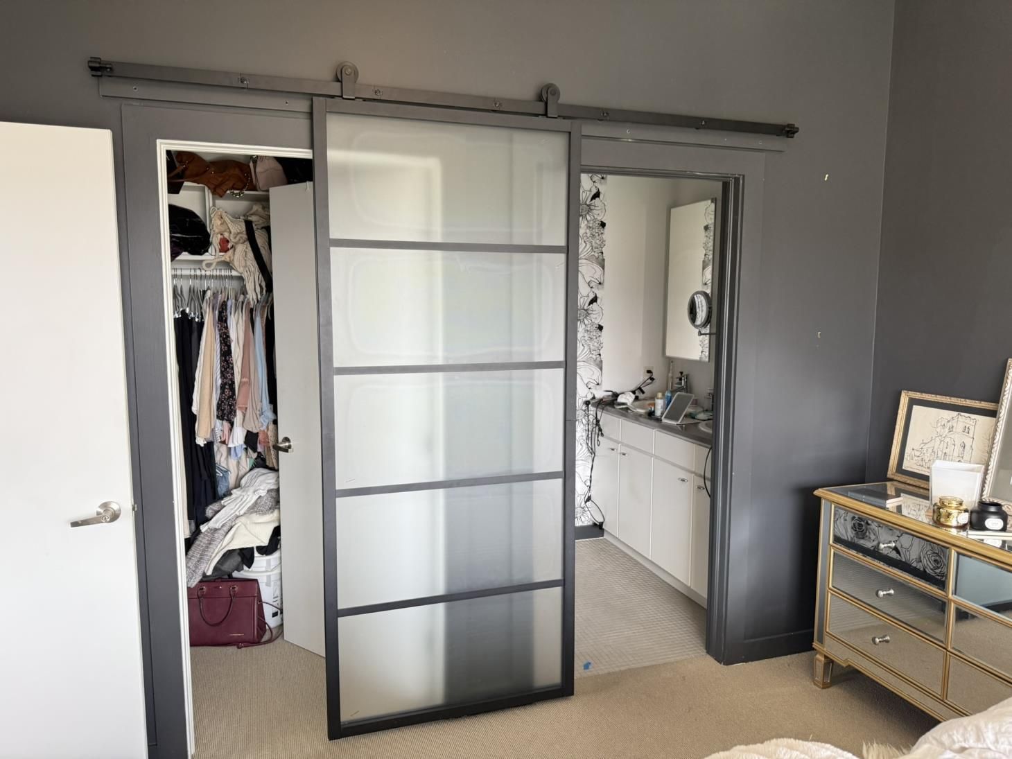 Gray metal-framed sliding glass doors open to a bathroom and closet in a bedroom.