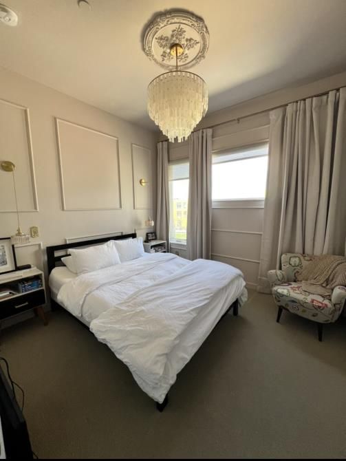 Bedroom with a bed, chair, and chandelier; neutral colors.