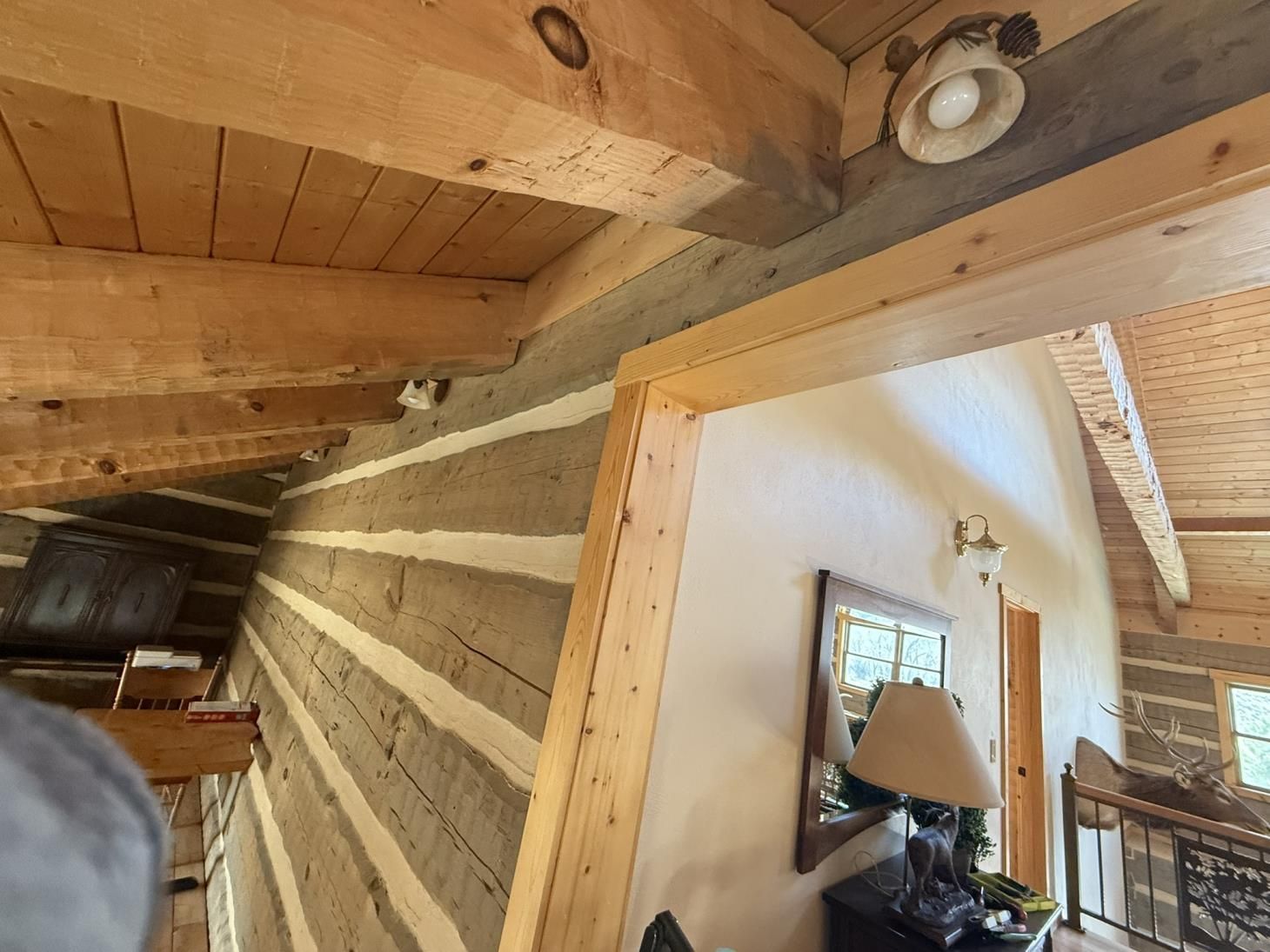 Interior view of a rustic cabin with log walls, wooden beams, and a doorway leading to a hallway.