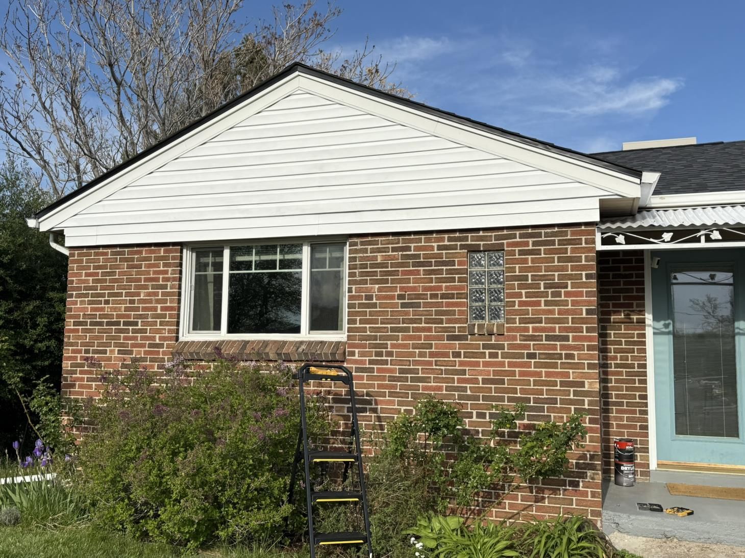 Brick house with white siding gable, white window trim, and a blue front door. A ladder rests against the brick.