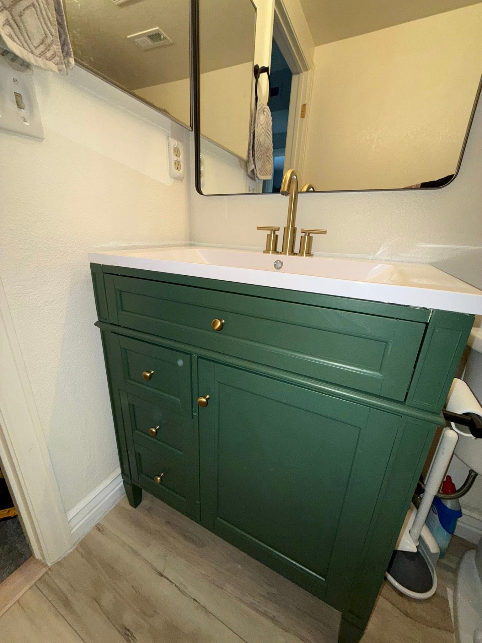 Green bathroom vanity with gold hardware, white countertop, and mirror.