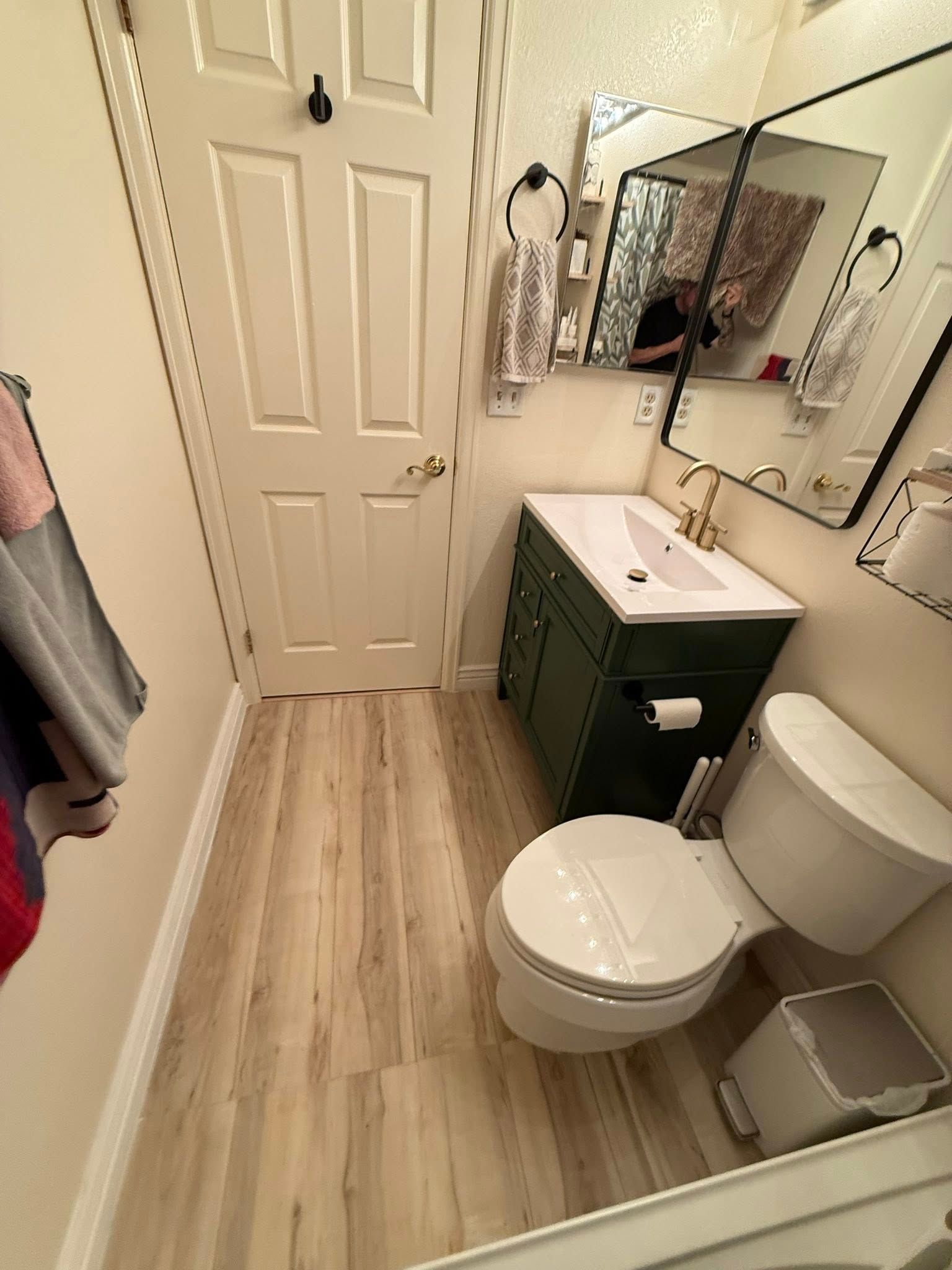 Small bathroom with green vanity, white toilet, and light wood-look flooring.