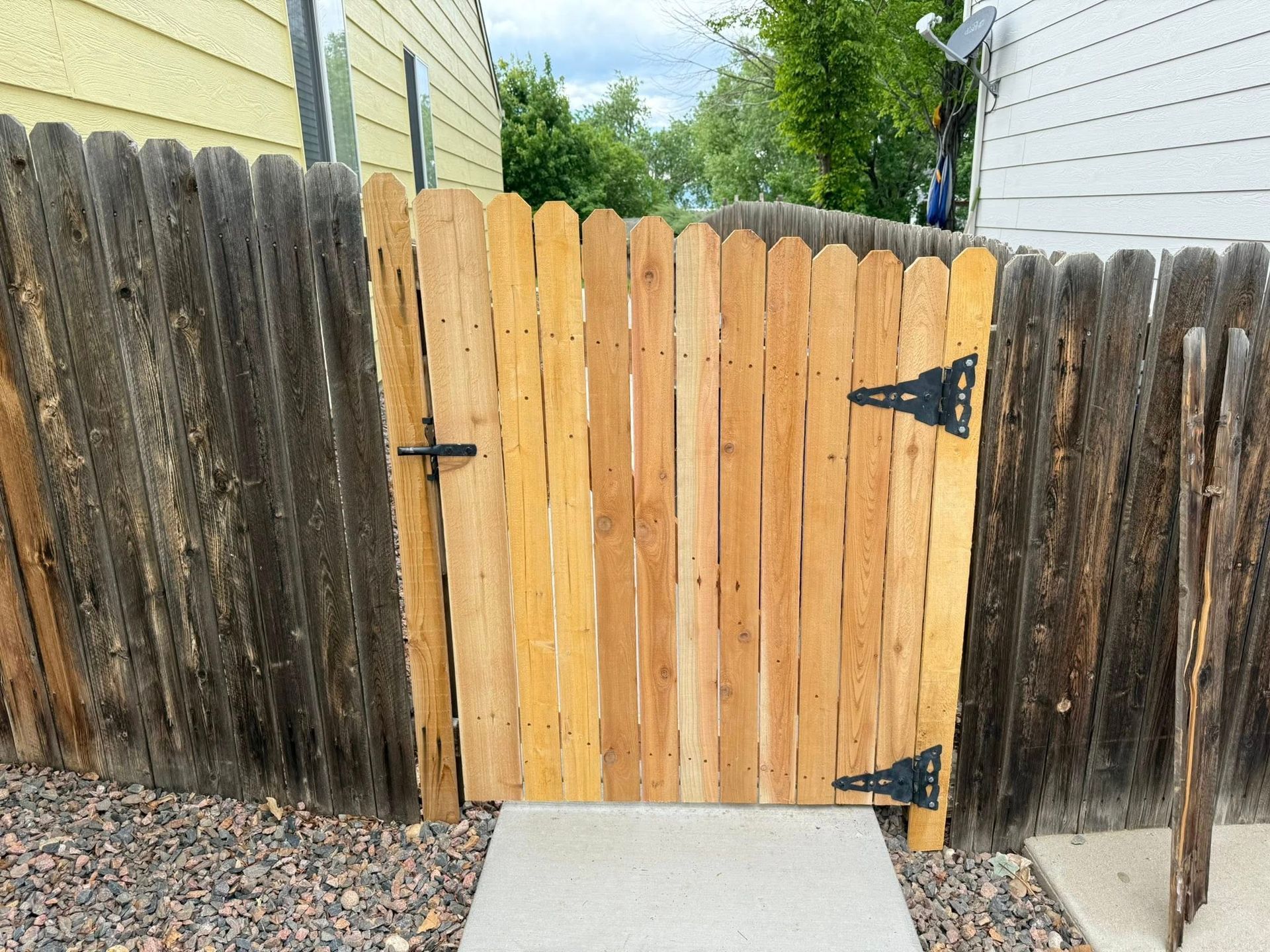 Wooden gate in a weathered fence, leading to a concrete walkway.