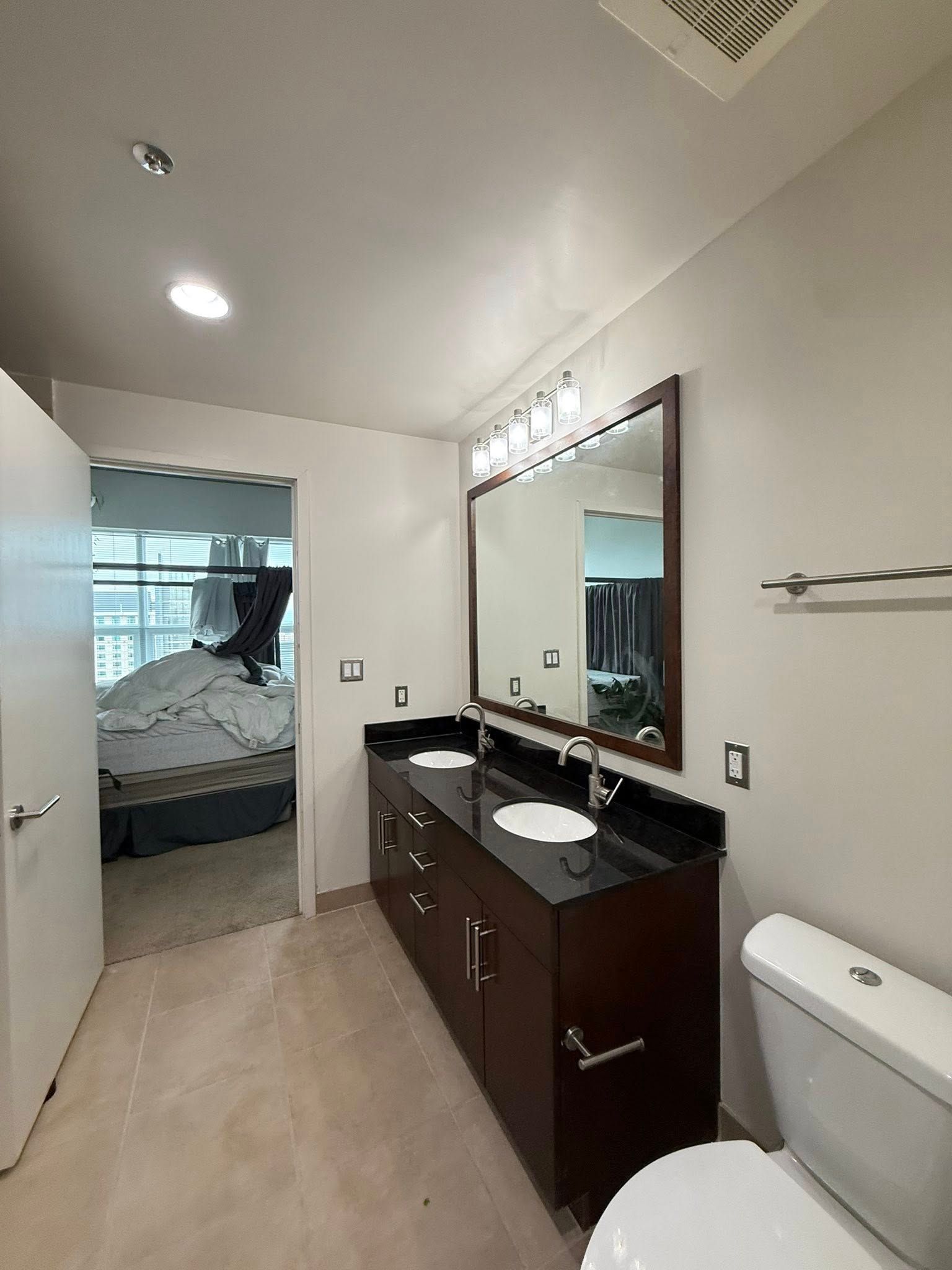 Bathroom with dark wood vanity, double sinks, large mirror, and open door to a bedroom.