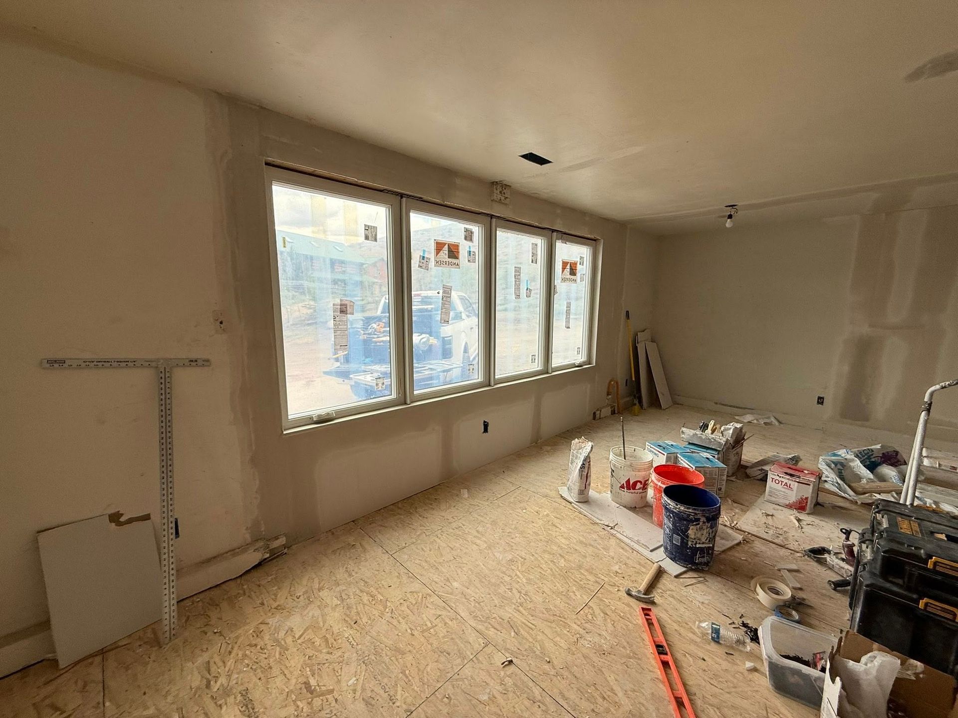 Room under construction with large windows, unfinished walls, and scattered tools.