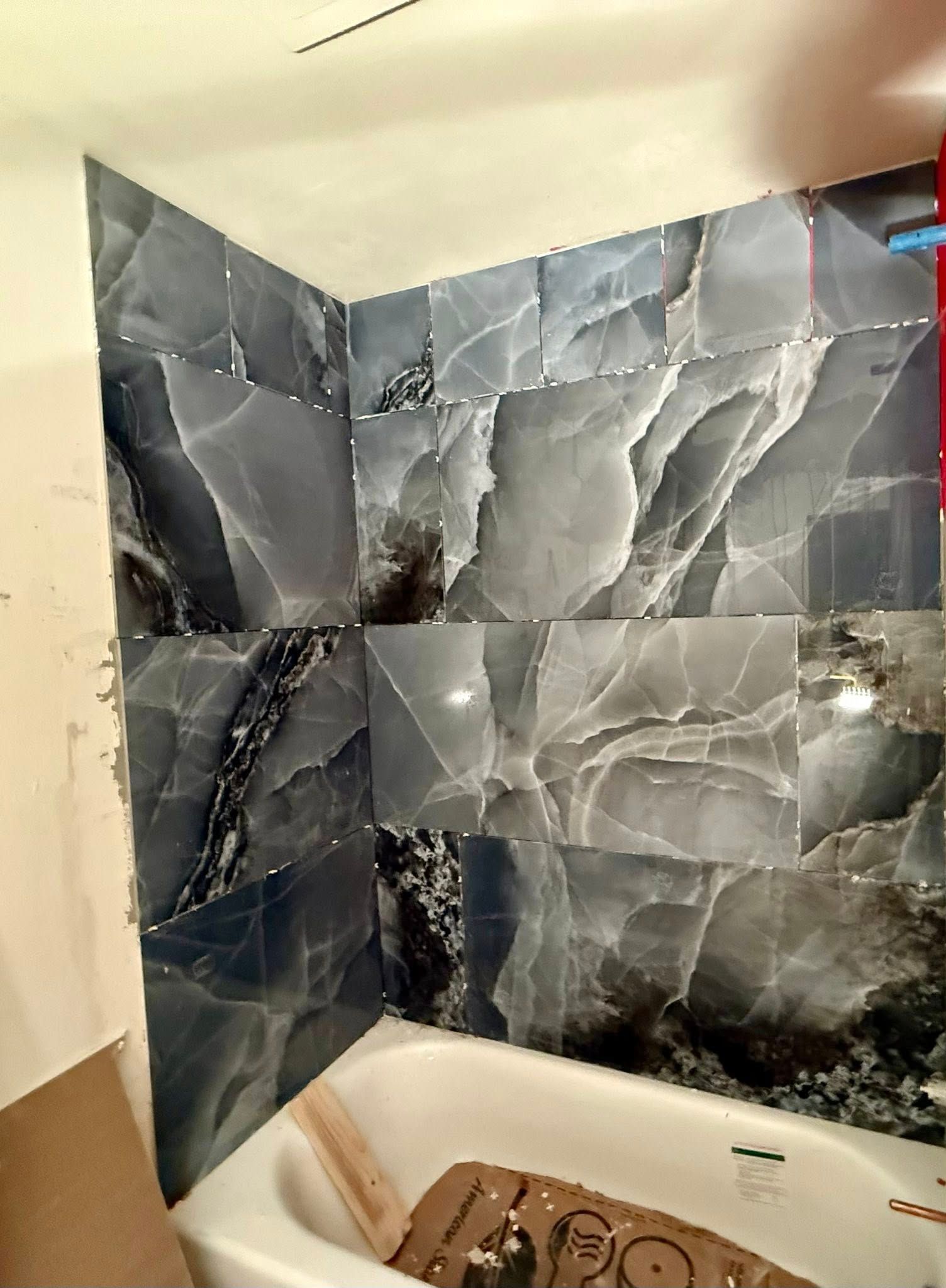 Bathroom corner with blue and gray marble-look tiles, unfinished drywall, and a white bathtub.