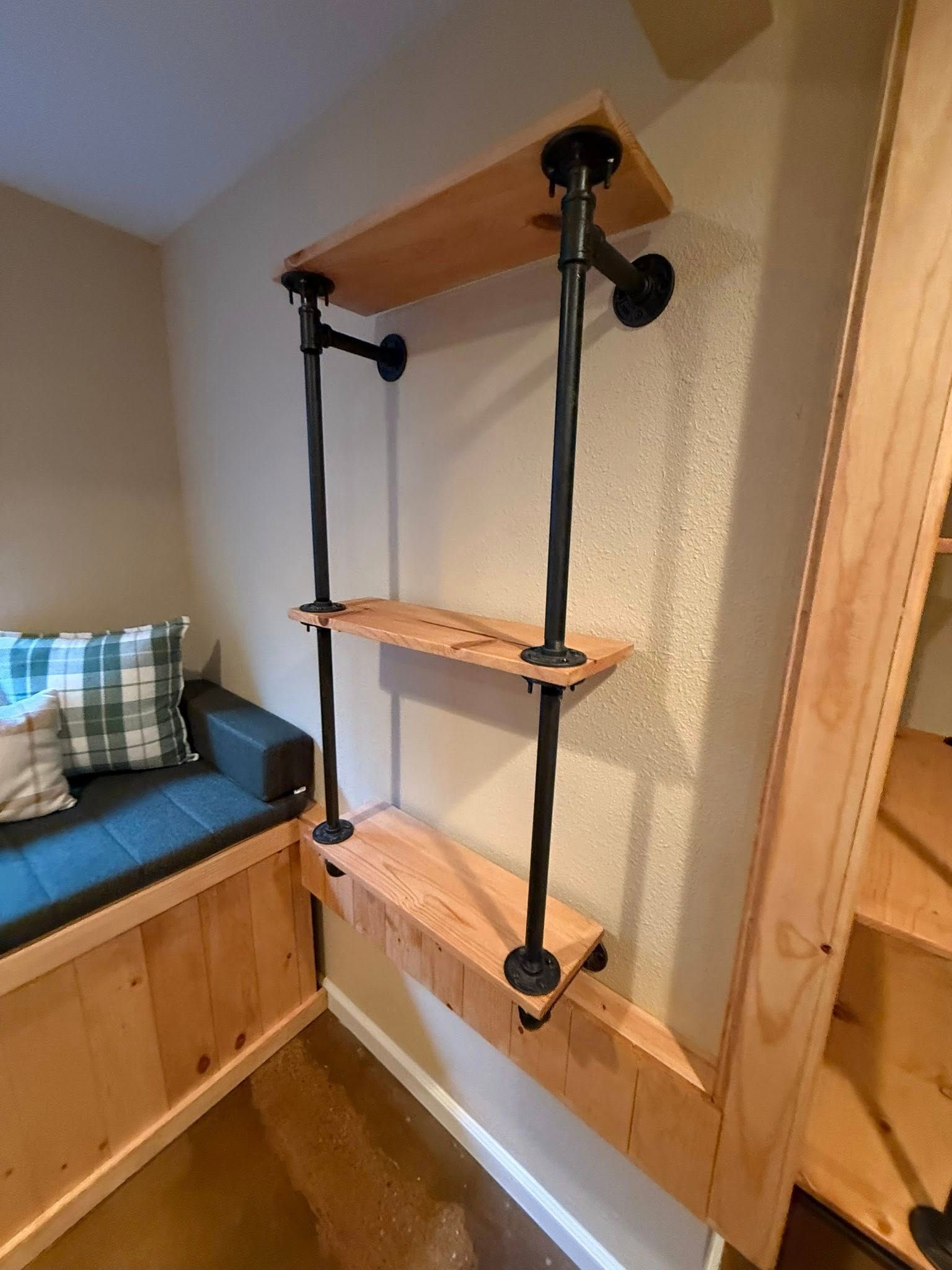 A wooden shelving unit with black pipes against a wall with a built-in bench.