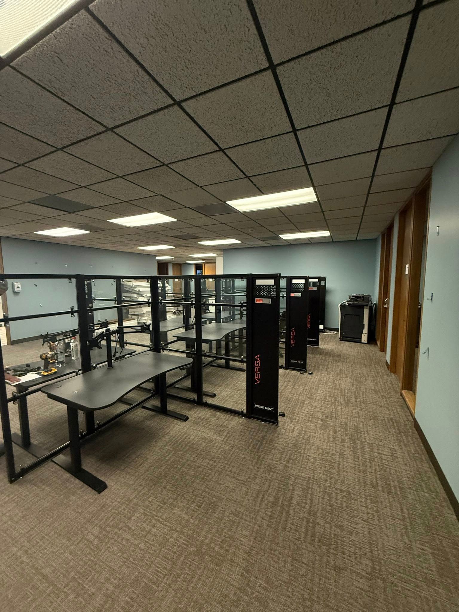 Office cubicles with desks and dividers. Beige carpet and patterned ceiling tiles.