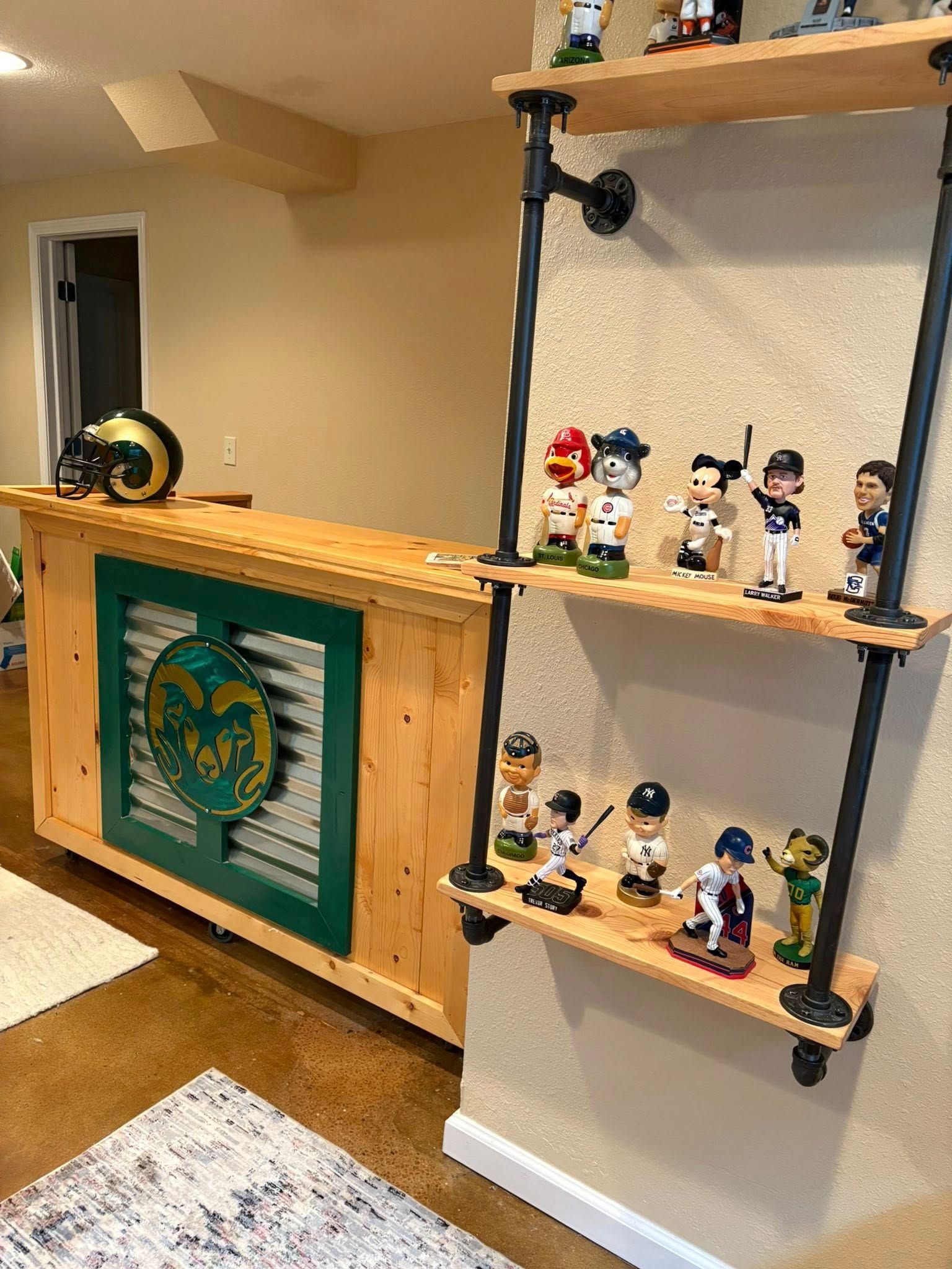 Bar with Rams logo and bobblehead shelves. Wooden bar with green accent. Bobbleheads on pipe shelves.