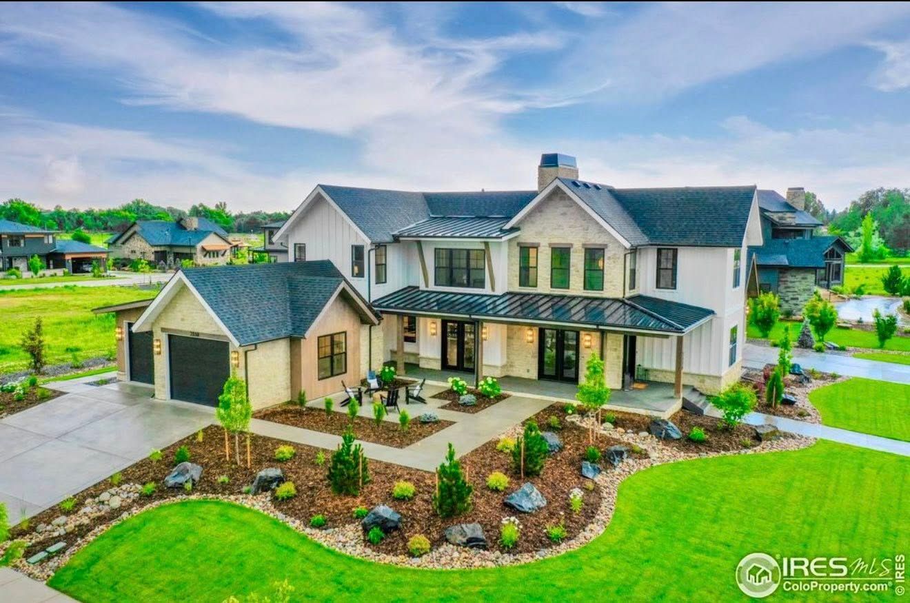 Two-story modern home with stone accents, black roof, and manicured lawn.