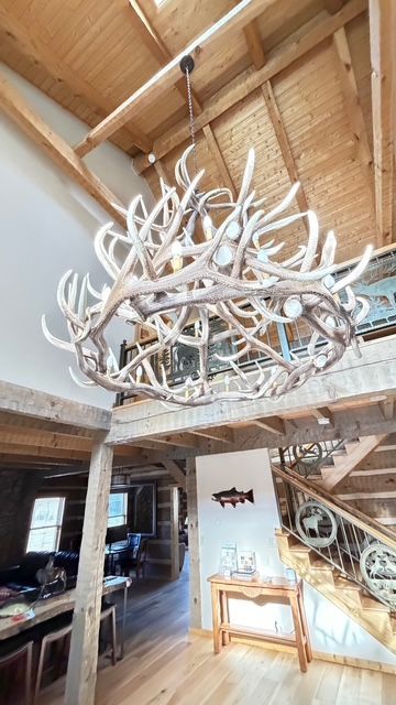 A large antler chandelier hangs in a rustic, wood-paneled interior above a staircase.