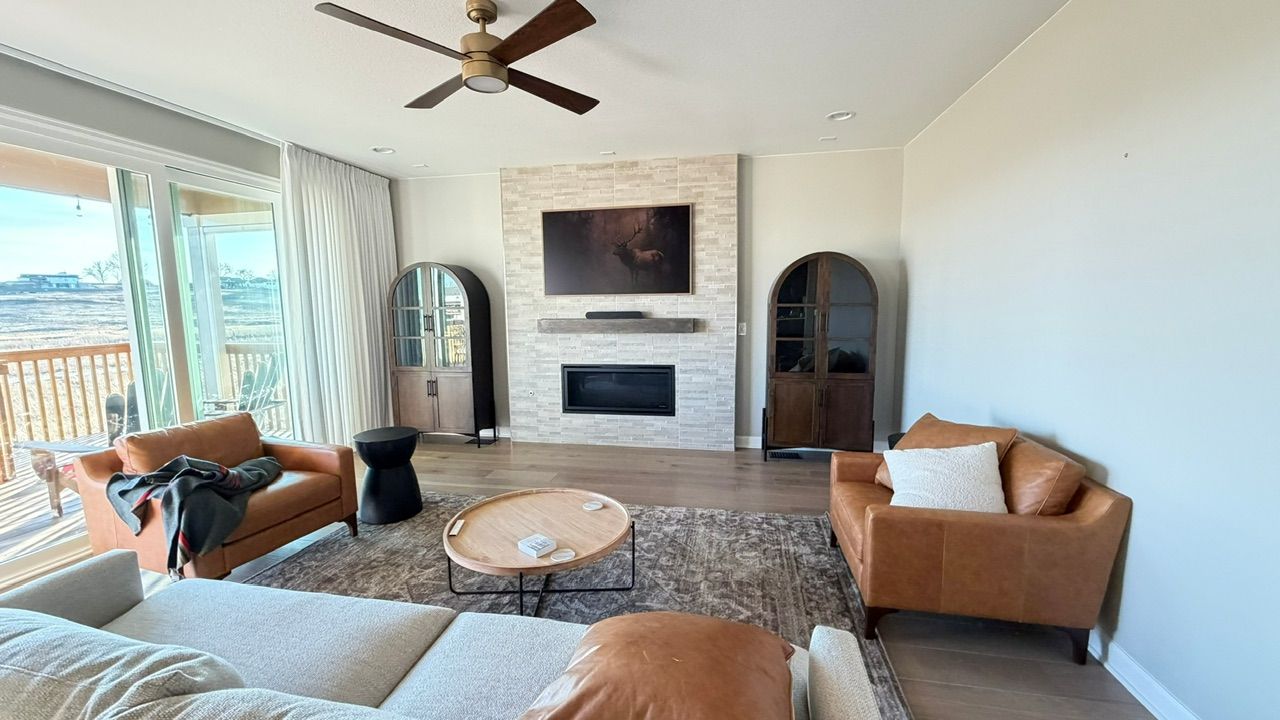Living room with tan leather chairs, fireplace, TV, and large windows with mountain view.