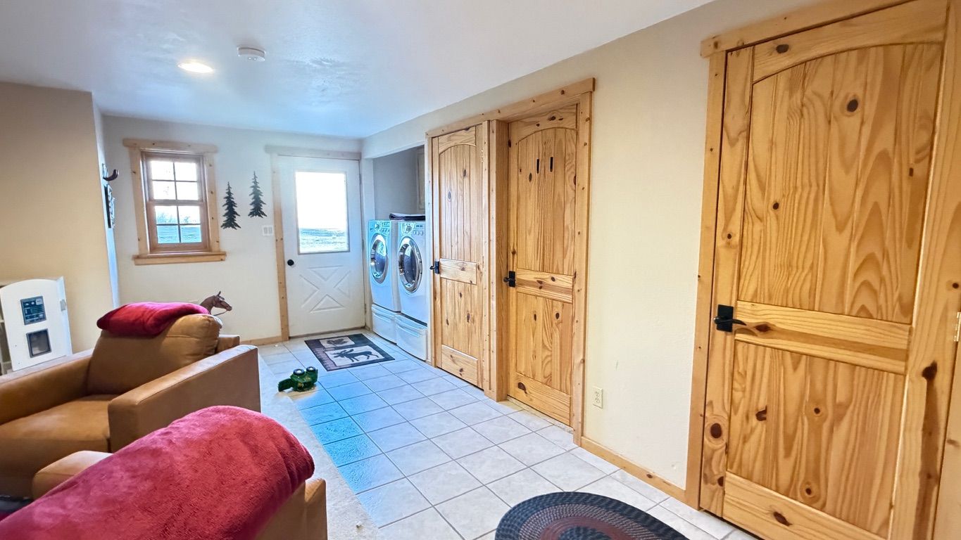 Laundry room with two wooden doors, a window, and a washer/dryer. Two armchairs are visible.