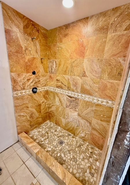 A shower with textured brown tile walls, pebble floor, and decorative mosaic band; unfinished trim.