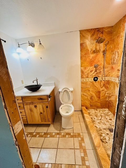 Bathroom with stone shower, wooden vanity, black sink, and toilet; beige tile floor.