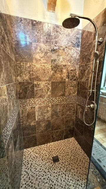 Tiled shower with pebble floor, dark brown marble walls, silver showerhead, and a mosaic accent.