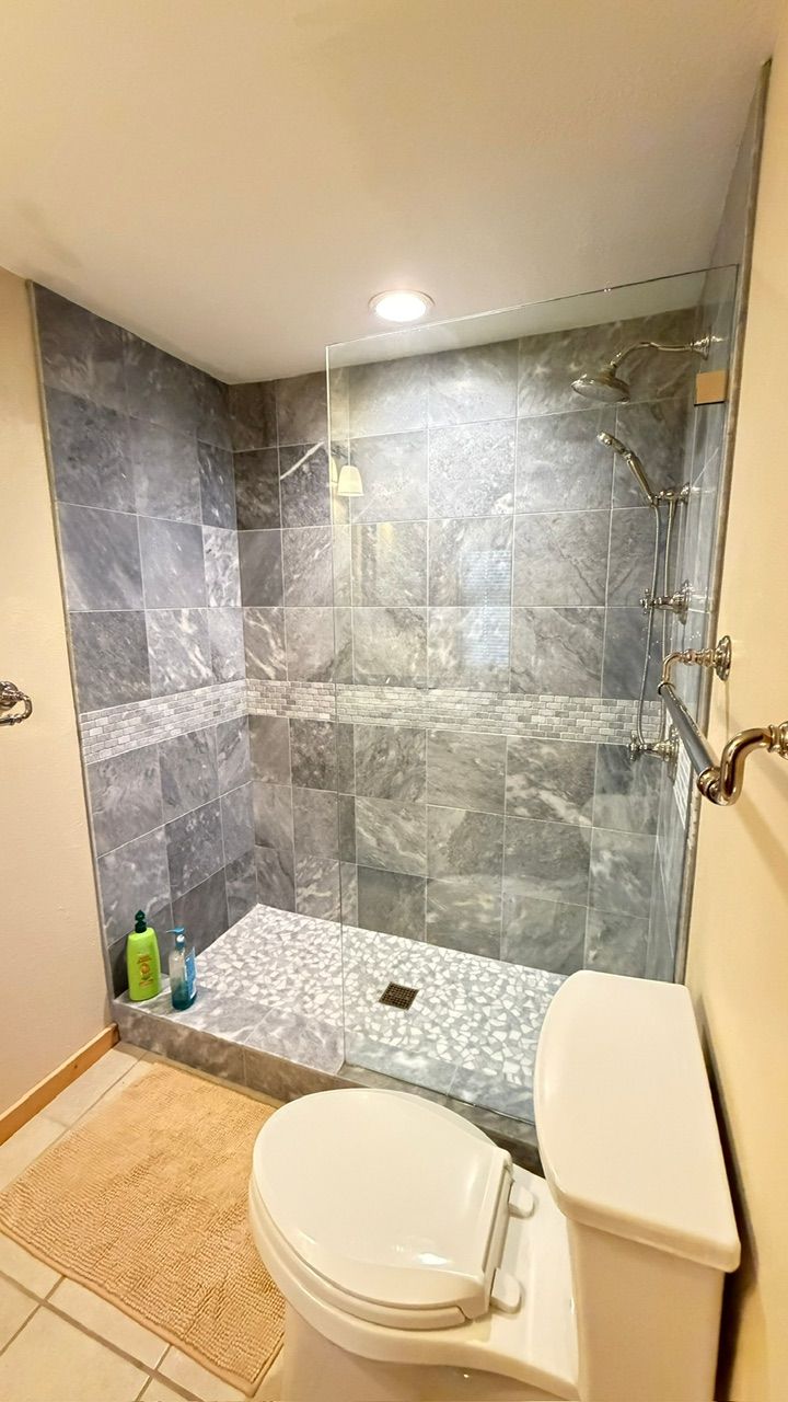 Bathroom with gray tiled shower, glass door, and white toilet.