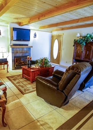 Cozy living room with fireplace, TV, and brown leather recliner. Wooden ceiling, tiled floor, and red coffee table.