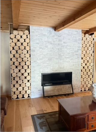 Fireplace with stacked logs on sides, gray brick, and wooden floor. A coffee table is in foreground.