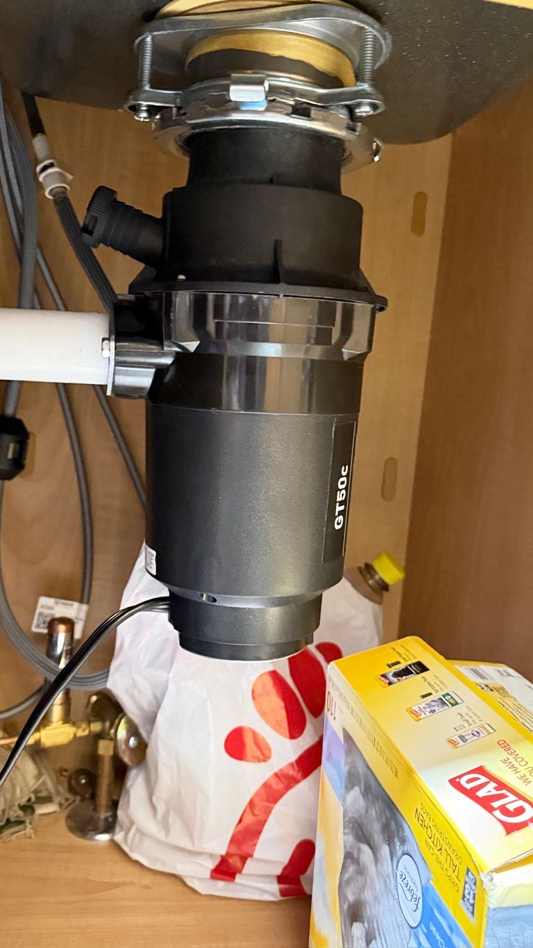 Garbage disposal unit under a kitchen sink, with attached pipes and electrical cord.