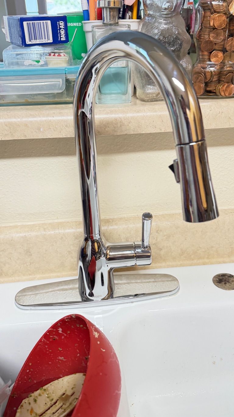 A chrome kitchen faucet over a white sink, with a red bowl in the foreground.