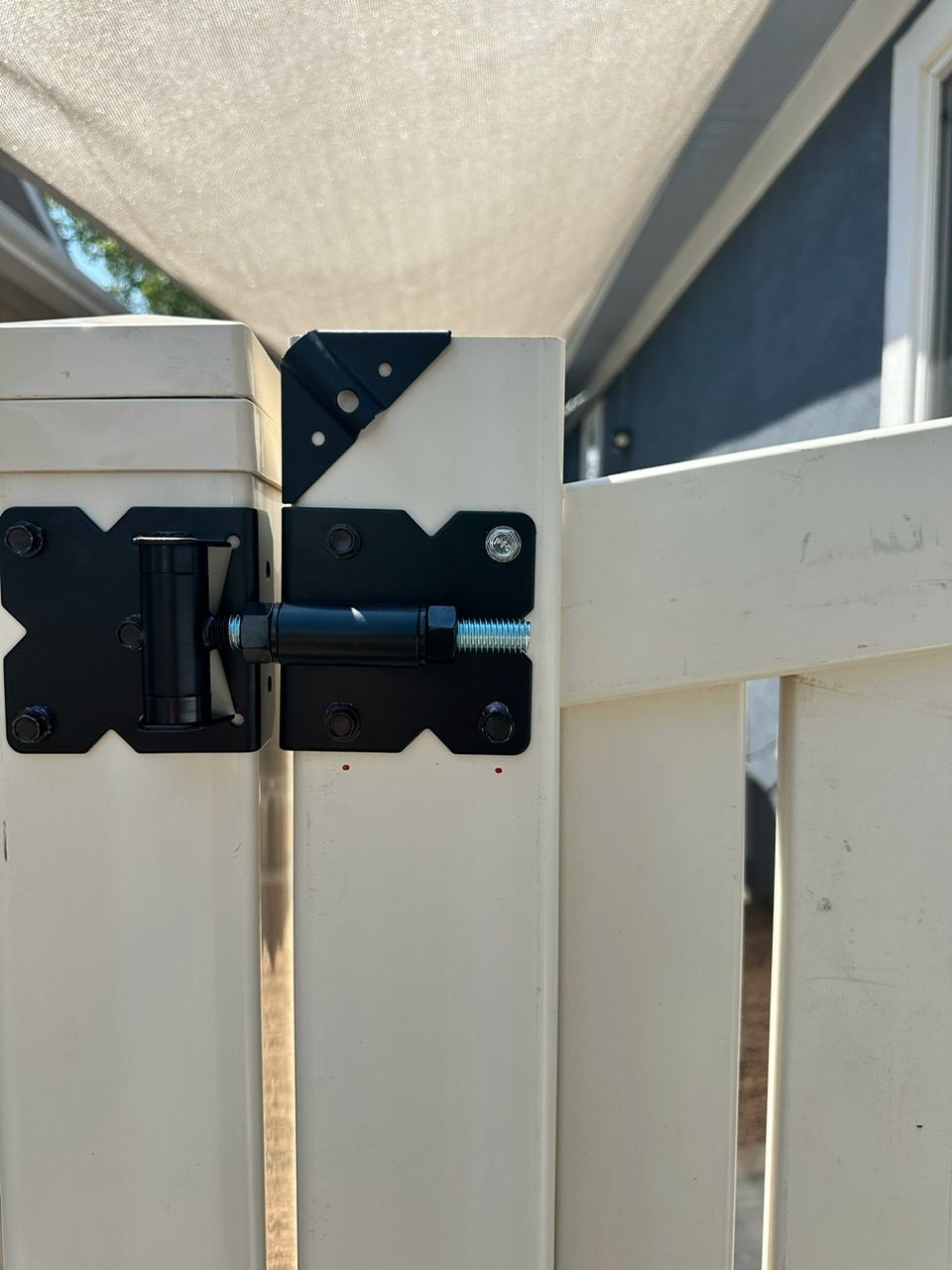 Black gate latch and corner brace on a white fence, secured with bolts.