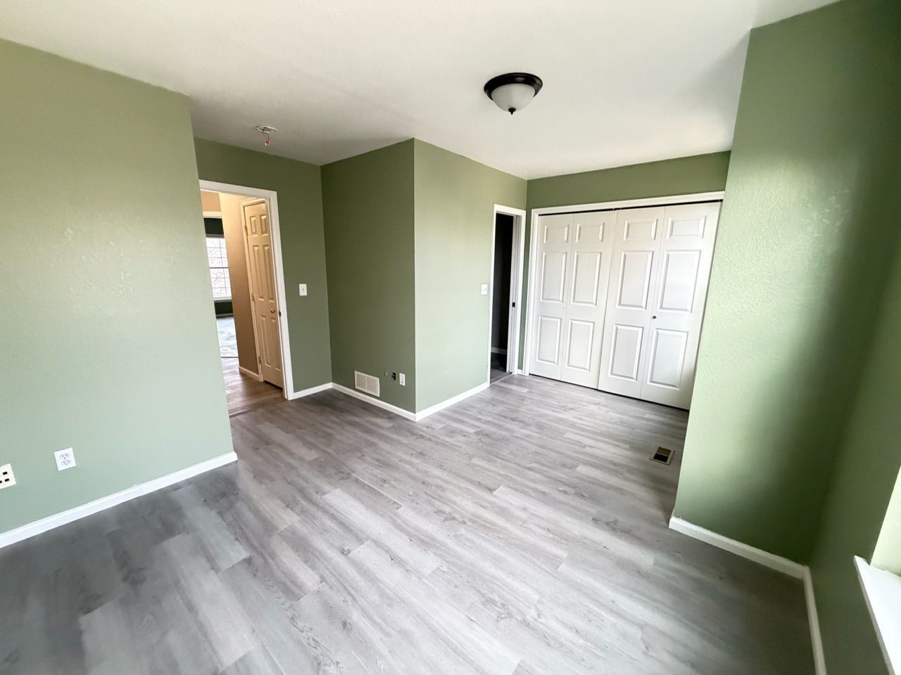 Empty room with light gray flooring and green walls, white closet doors, and a small light fixture.