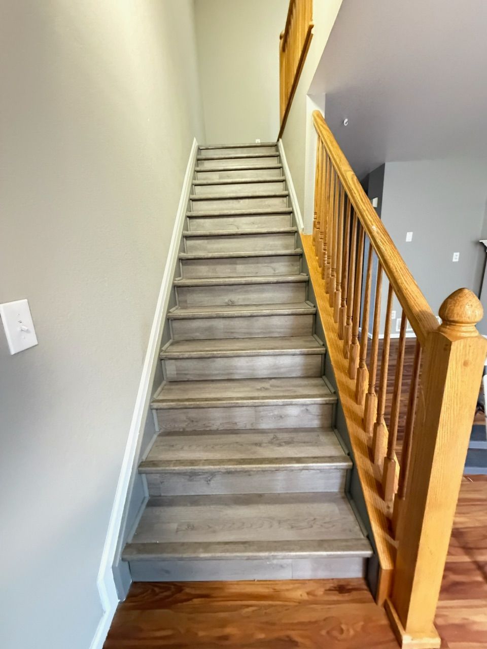 Staircase with wood and gray treads, wooden banister, and light gray walls.
