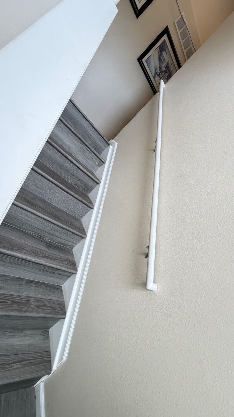 Staircase with gray wooden steps, white handrail along the wall, and tan wall.