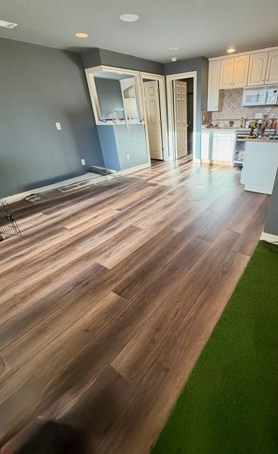Room with hardwood floors, blue wall, white cabinets, and a green patch of flooring.
