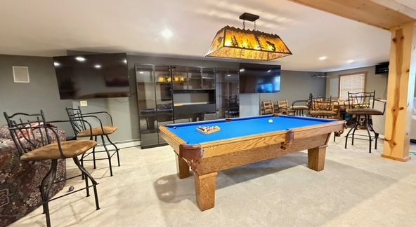 Game room with pool table, bar stools, and two TVs on a gray wall.