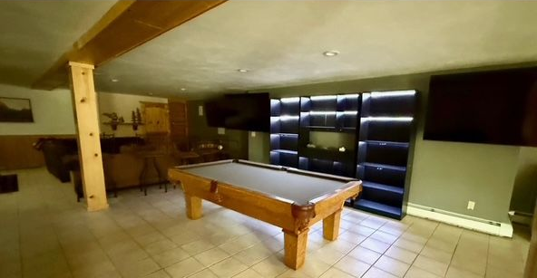 A pool table in a basement game room with shelves, TV, and wooden beams.