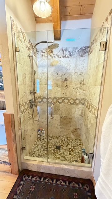 Shower with glass doors, beige tile, pebble floor, and multiple showerheads.