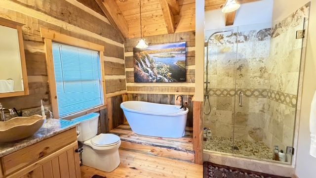 Rustic bathroom with a clawfoot tub, glass shower, wooden vanity, and log walls.