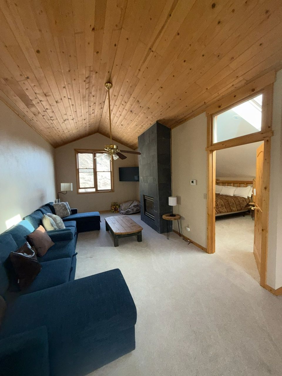 Living room with blue sectional sofa, fireplace, wood ceiling, and bedroom doorway.