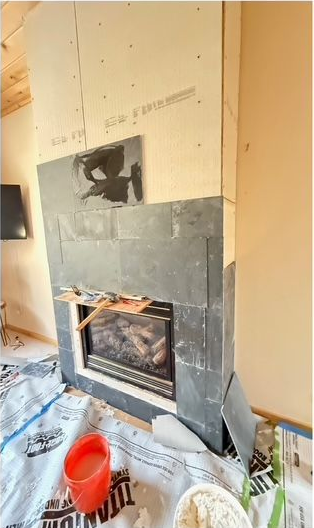 Fireplace under construction, covered in slate tile. Tools and supplies on the floor.