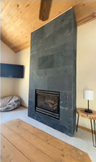 Modern fireplace with black tile surround, in a cabin-style room with a wood ceiling, TV, and table.
