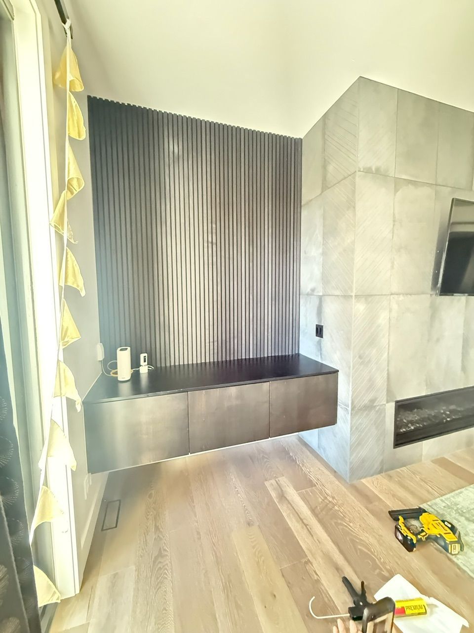 Floating media cabinet beneath textured dark wall, next to a stone fireplace. Wooden floors and curtains.