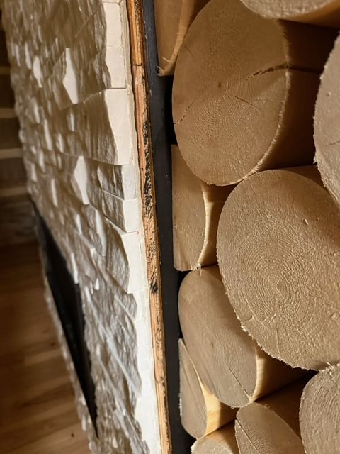 Close-up of a stack of light-colored, circular wooden logs next to a textured, white-painted wall and dark trim.