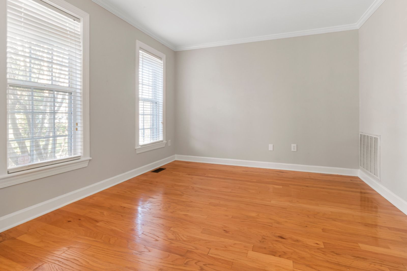 Empty room with hardwood floors, two windows, and light gray walls.