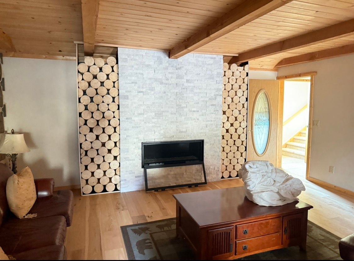 Living room with fireplace flanked by log storage, white brick, and a wood ceiling.