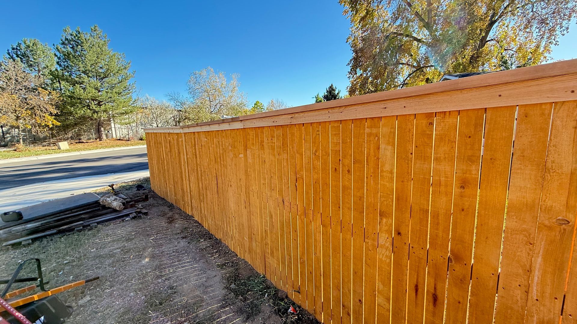 Wooden fence curving alongside a street on a sunny day.